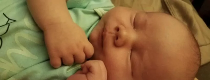 Sleeping newborn baby in mint onesie.