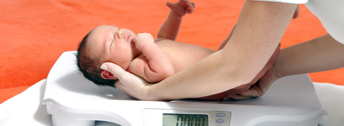 Newborn baby being weighed on scale.