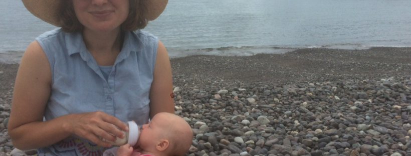 Mother bottle-feeding baby on rocky beach.