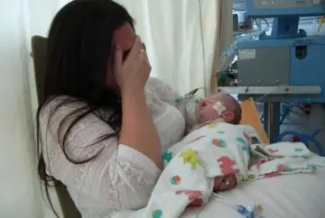 Distressed mother holding sick infant in hospital.