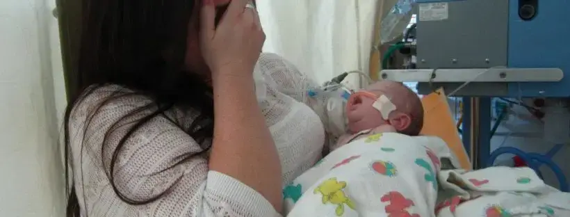 Distressed mother holding sick infant in hospital.