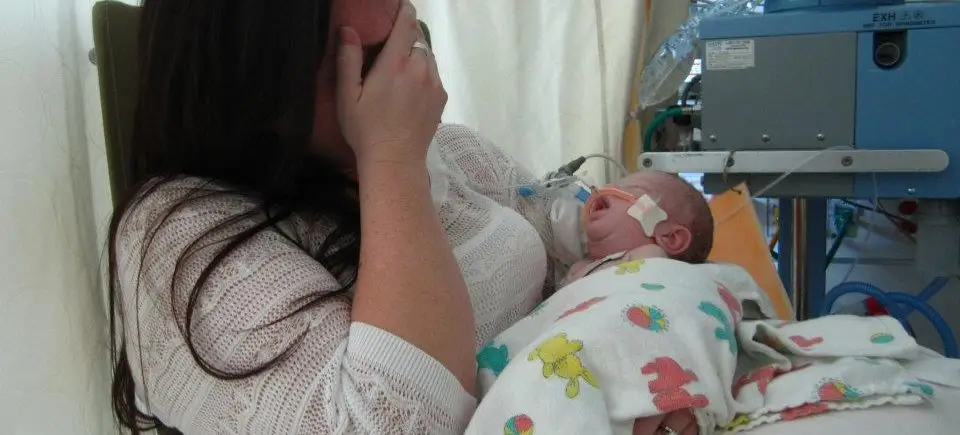 Distressed mother holding sick infant in hospital.