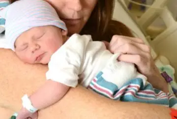 Newborn baby sleeping on mother's shoulder.