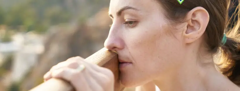 Woman pensively holding wooden railing.