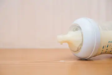 Baby bottle with milk spilling on table.