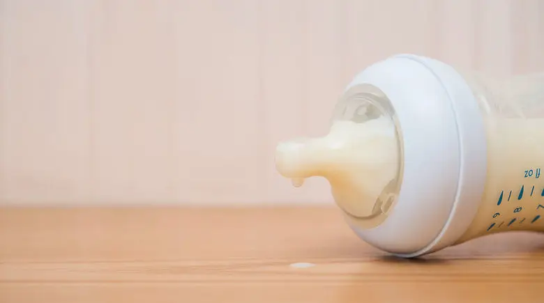 Baby bottle with milk spilling on table.