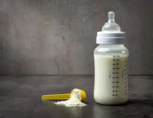 Here's an alt tag for the image: Baby bottle with formula and scoop.