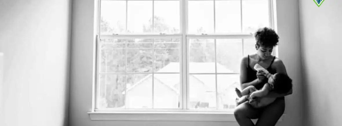 Mother bottle-feeding baby by window.