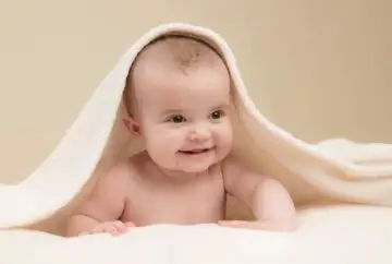 Smiling baby under white towel.